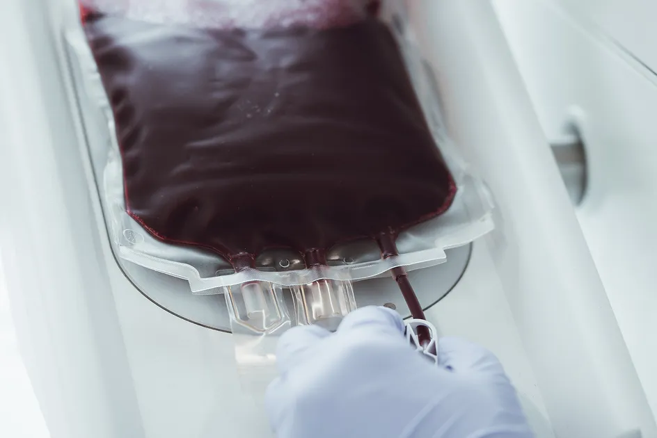 A hand wearing a white glove holds a blood bag in a medical device.