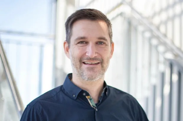 Smiling man with a beard standing in a modern, bright room.