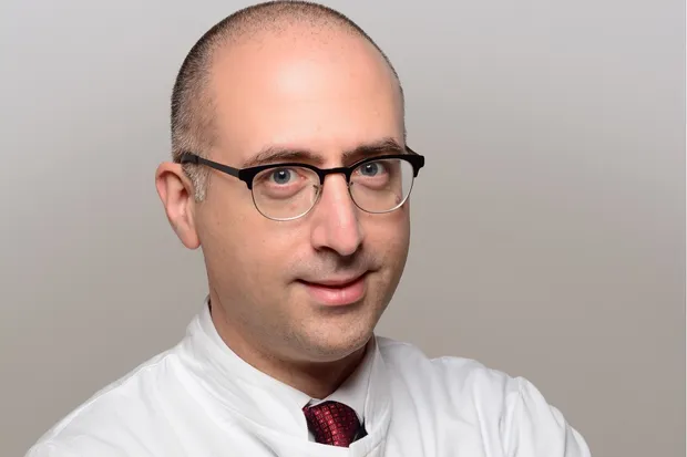 Picture is showing men with glasses and a dark suit - Prof. Dr. med. Dimitrios Mougiakakos - standing in the hallway of the Magdeburg Oncology Center