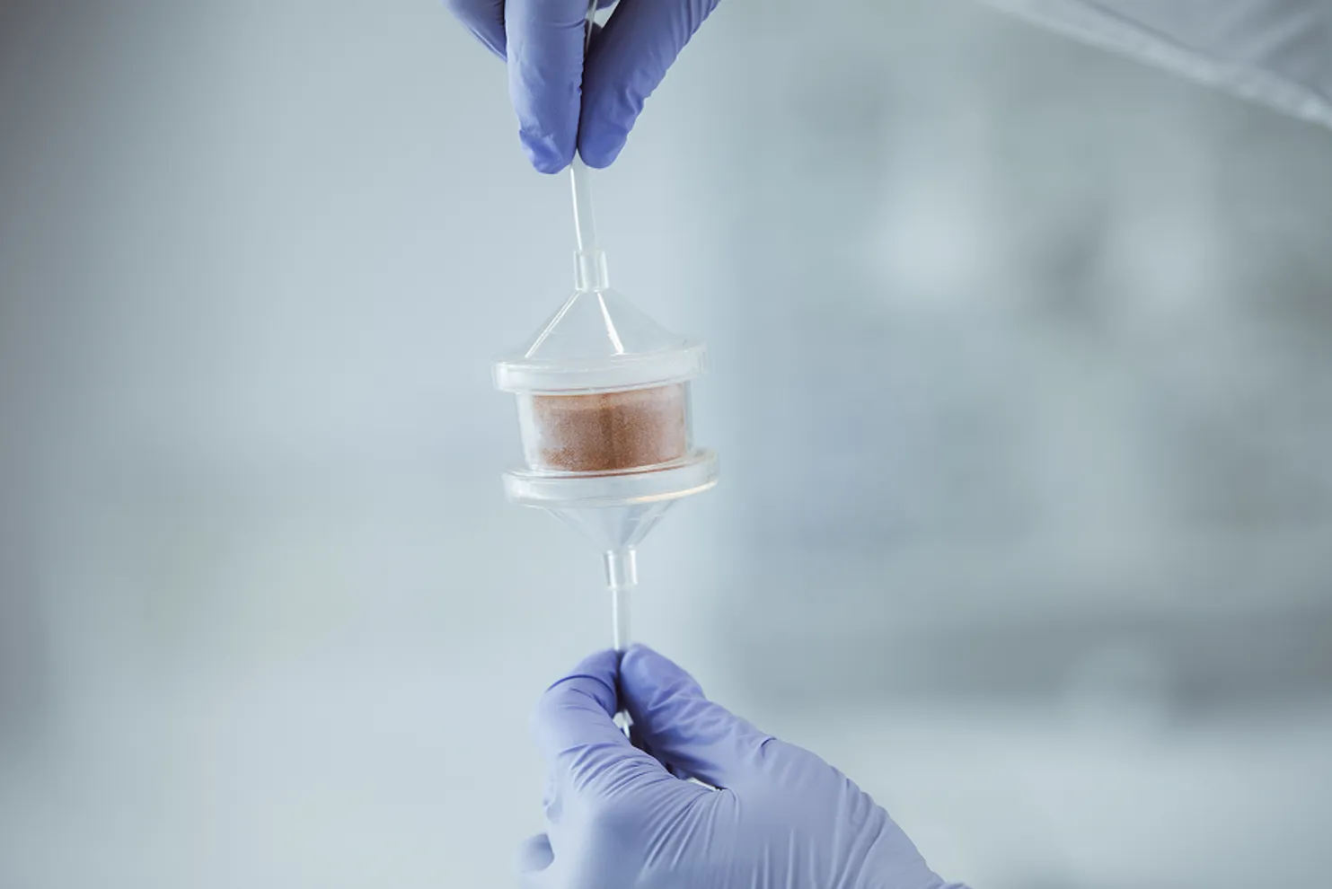 Hands wearing blue gloves holds a container with a sample.