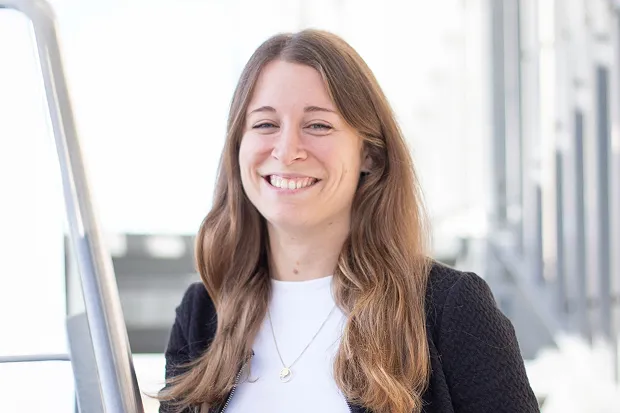 Smiling woman with long, curly hair standing in front of a bright, modern background.